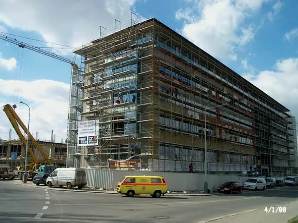 Rozsáhlé fasádní lešení na administrativní budově se žlutým vozem
